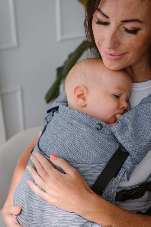 Modelka nosi dziecko w ergonomicznym nosidle KAVKA multi-age ink twill - niebieskie nosidlo z delikatnym wzorem w jodelke (a blue carrier with a twill delicate herringbone pattern)