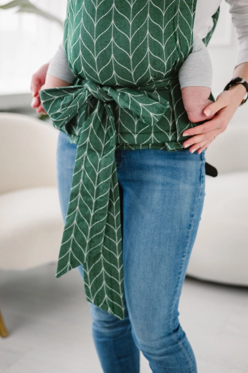 Modelka-nosi-dziecko-w-ergonomicznego-nosidle-KAVKA-Handy-fern-braid-bamboo--zielone-nosidlo-z-bialym-wzorem-warkocza-green-braid--with-white-braid-pattern.webp