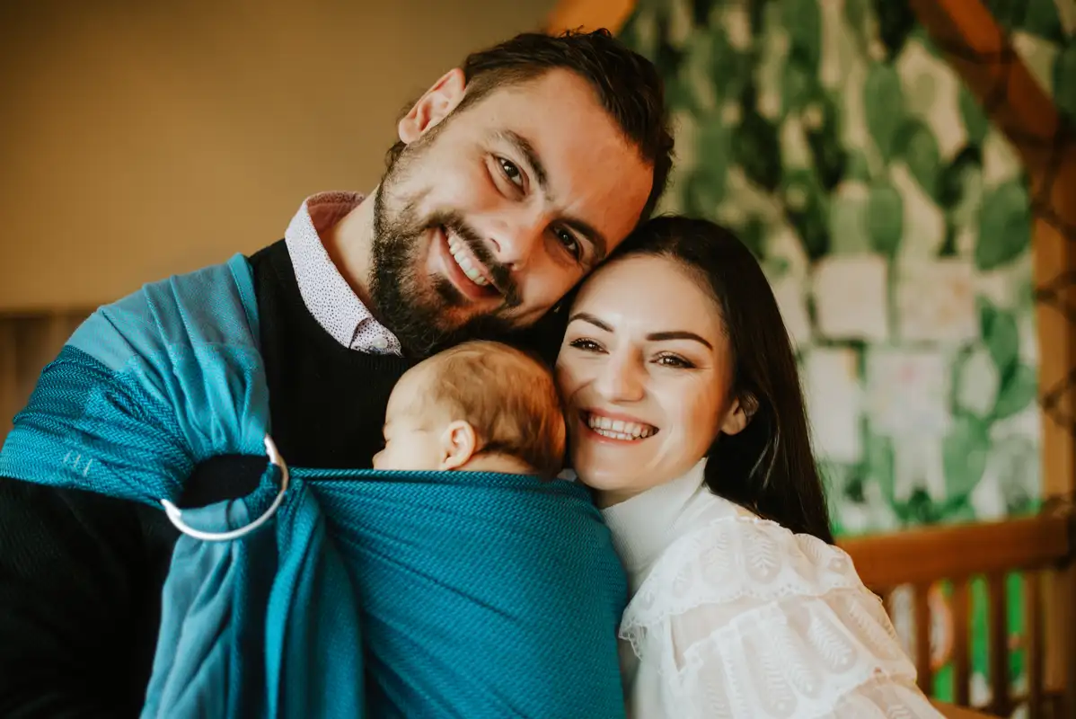 Mama nosząca niemowlę w chuście kółkowej w pozycji pionowej na biodrze